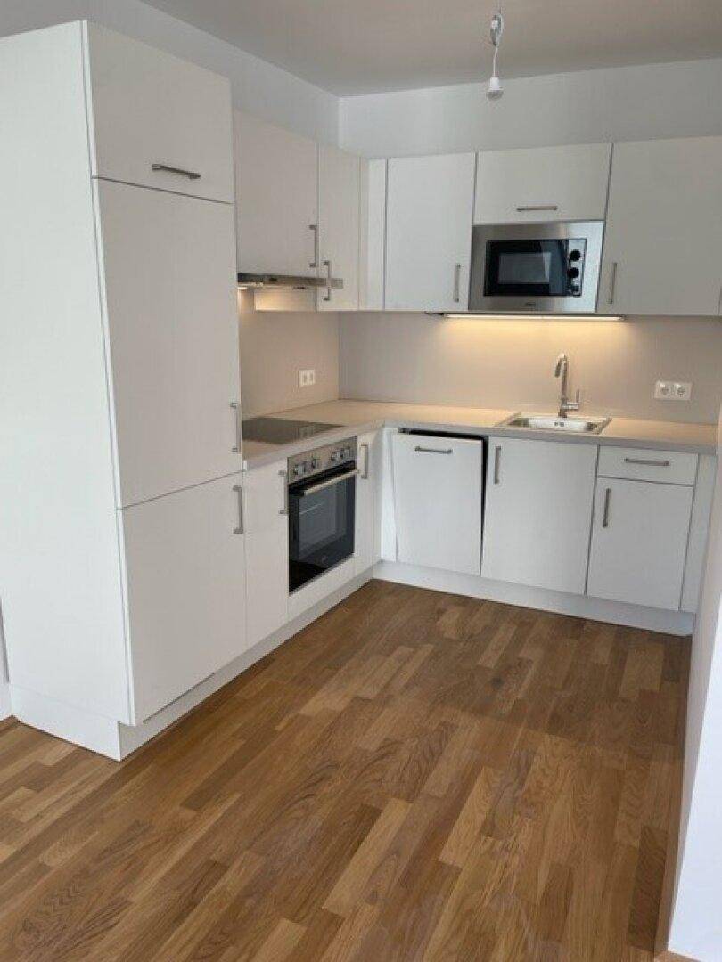 Moderne Einbauküche mit weißen Schränken, integrierten Geräten und Holzparkett.