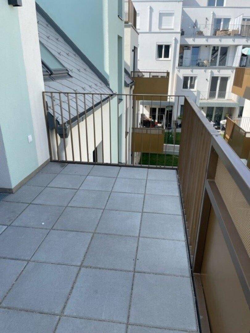 Heller Balkon mit Fliesen und Metallgeländer, bietet einen seitlichen Blick auf die Nachbargebäude.