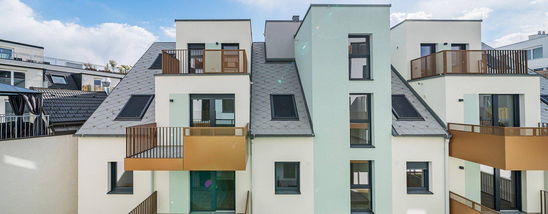 Ansicht der modernen Wohnanlage mit Satteldächern, Balkonen und Dachfenstern.