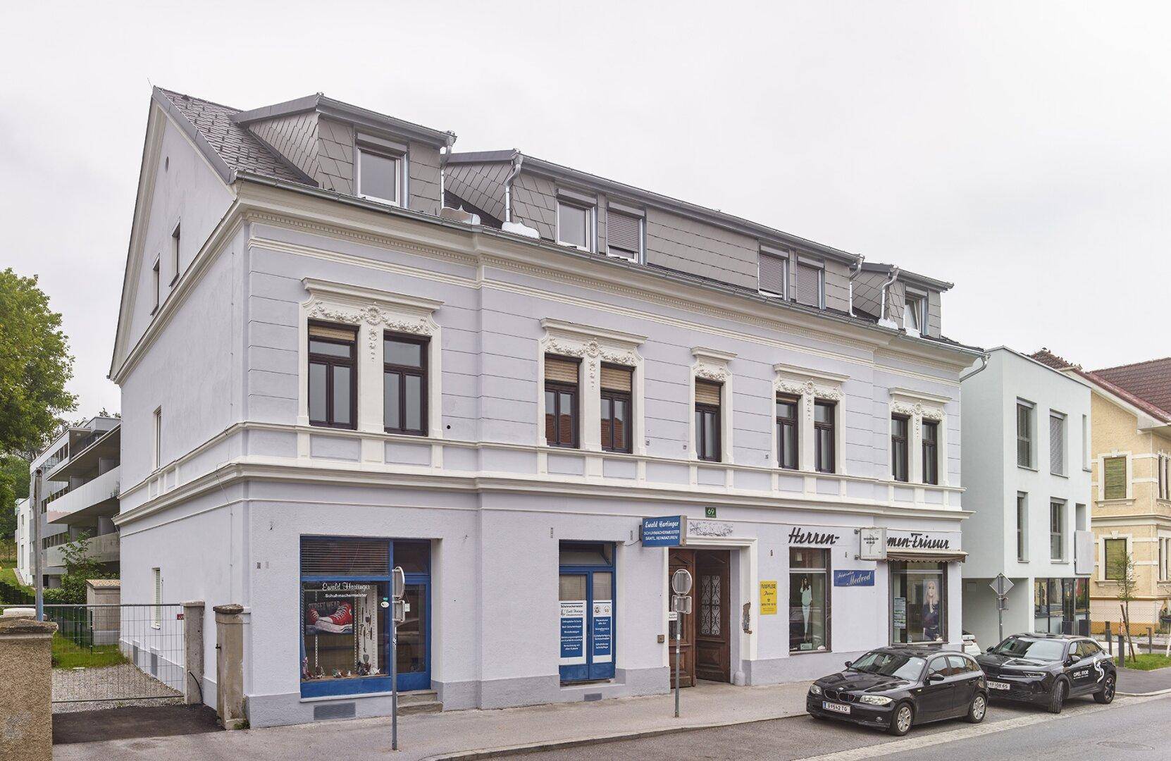 Gebäudefassade mit traditionellen Elementen und Geschäften im Erdgeschoss an einer belebten Straße.
