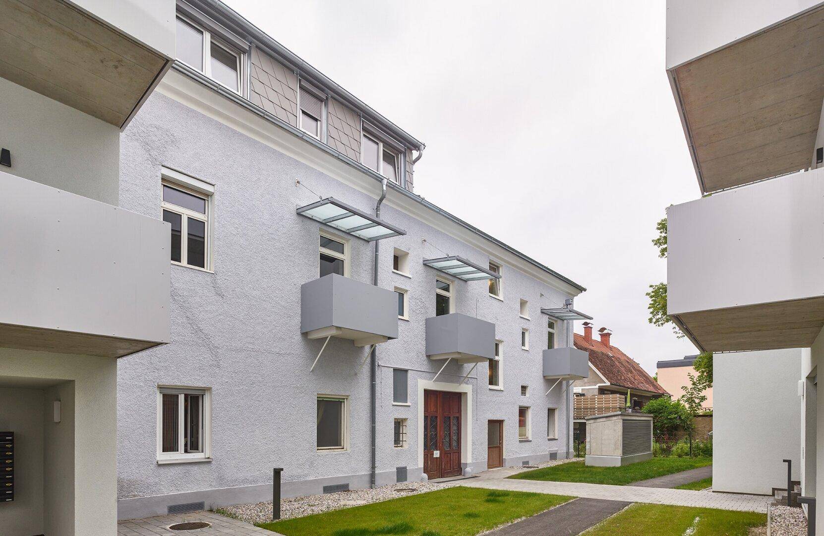 Außenansicht eines Wohnhauses mit kleinen Balkonen und einem gepflegten Zugangsbereich.