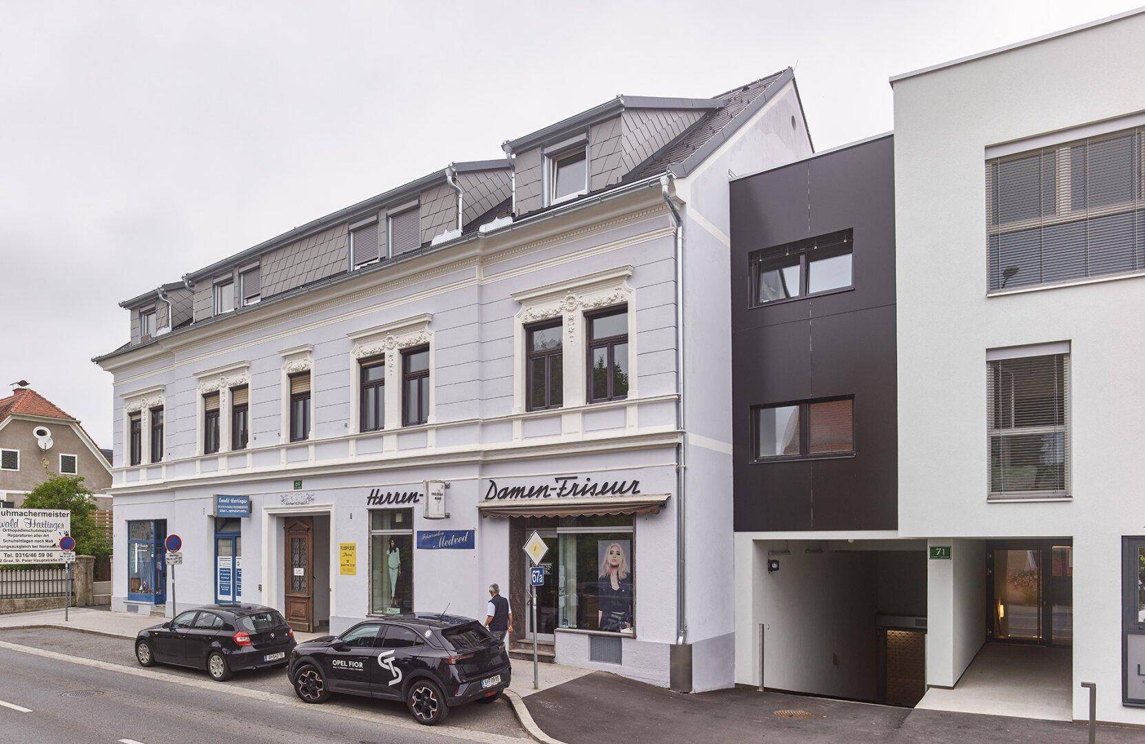 Renovierter Altbau mit Geschäften und angrenzendem modernen Neubau an einer städtischen Straße.