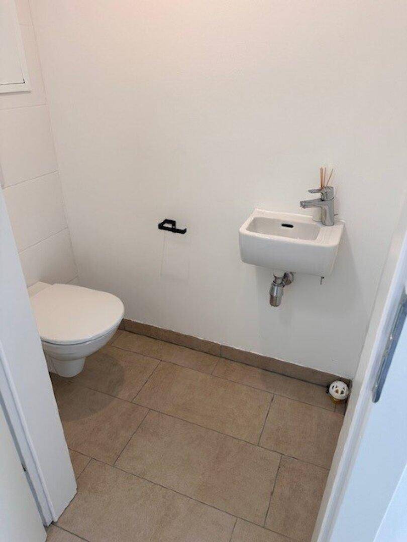 Kleines Gäste-WC mit Wand-WC, Waschbecken und hellen Fliesen.
