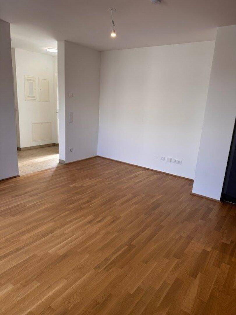 Geräumiger, leerer Wohnbereich mit hellem Parkettboden und weißen Wänden.