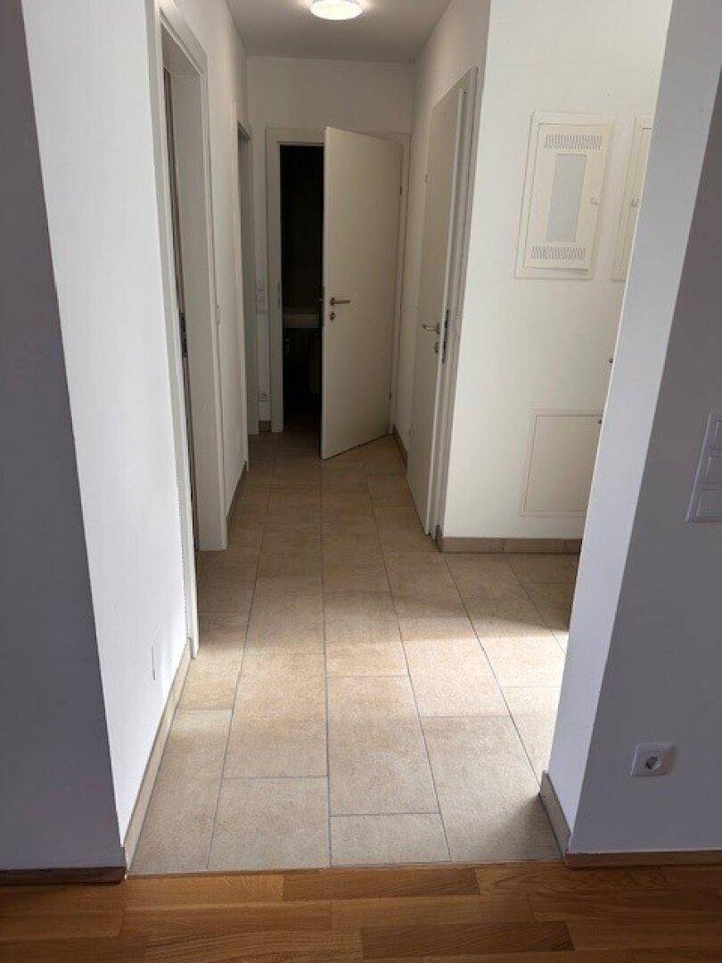 Heller Flur mit Fliesenboden, weißen Wänden und Zugang zu verschiedenen Räumen.