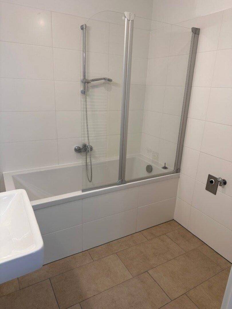 Badezimmer mit Badewanne inklusive Duschabtrennung und hellen Fliesen.