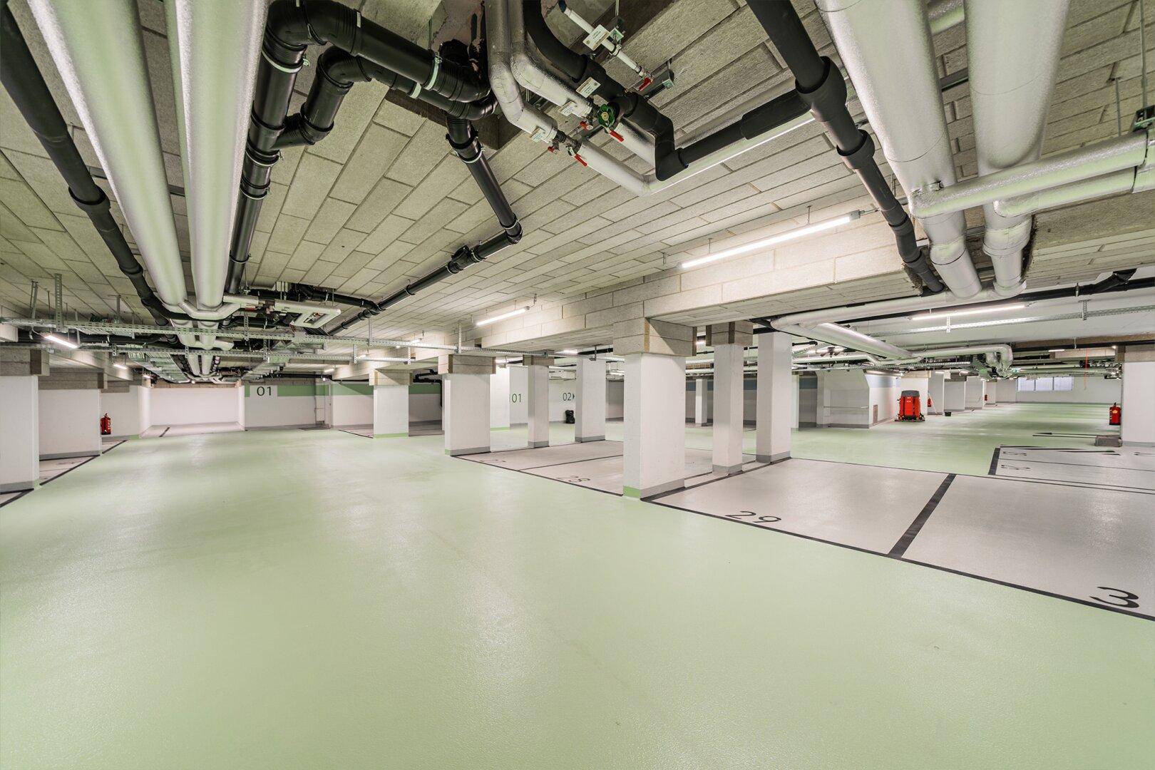 Geräumige Tiefgarage mit vielen Parkplätzen und sichtbaren Installationen an der Decke.