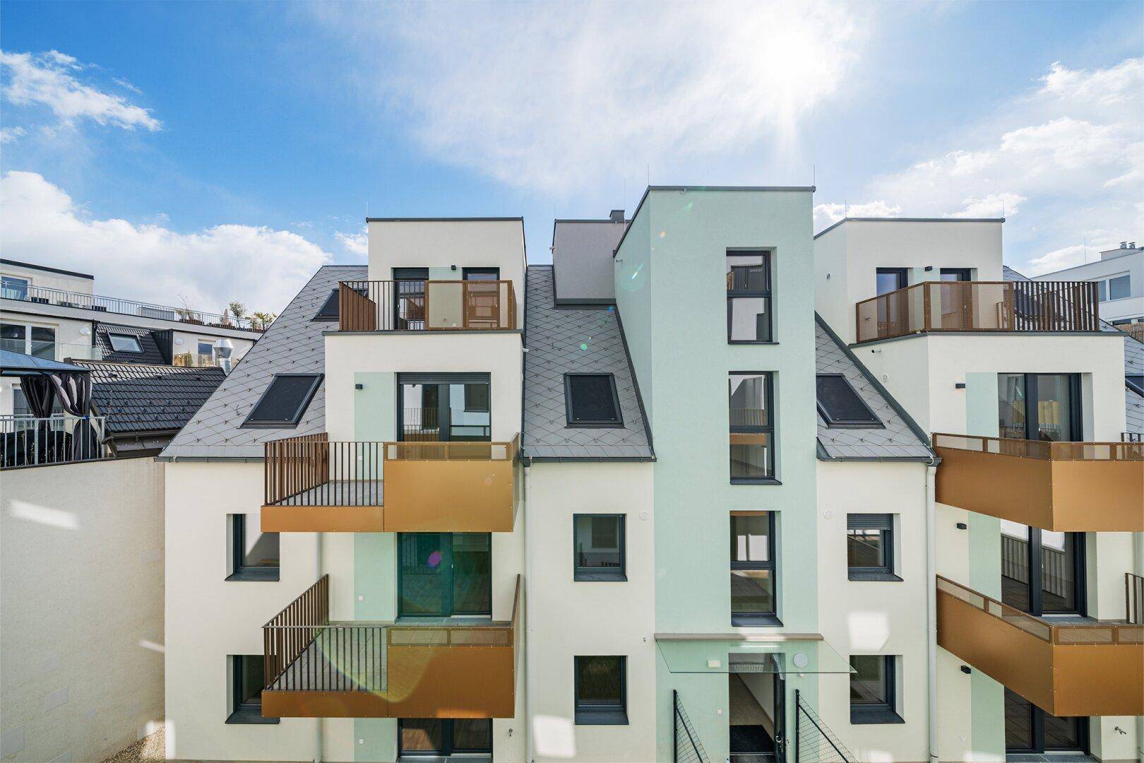 Moderne Wohngebäude mit Balkonen und Dachfenstern unter einem sonnigen Himmel.