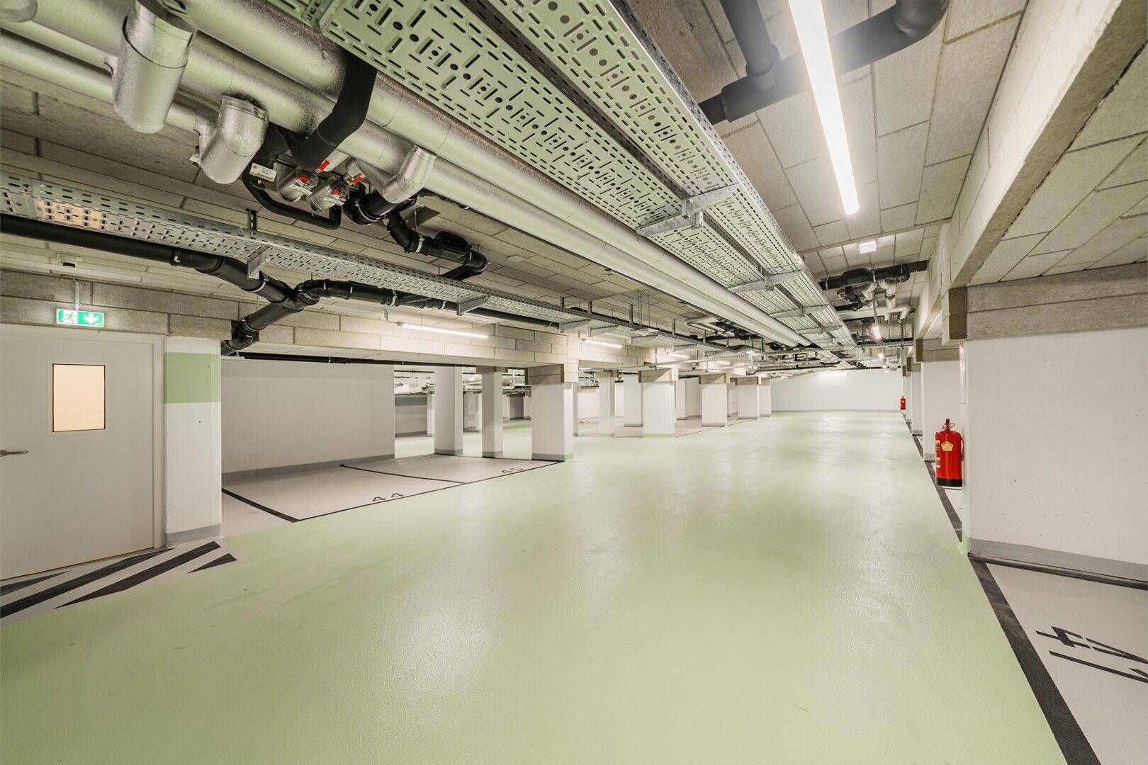 Weitläufige Tiefgarage mit hellgrünem Boden und modernen Beleuchtungssystemen.