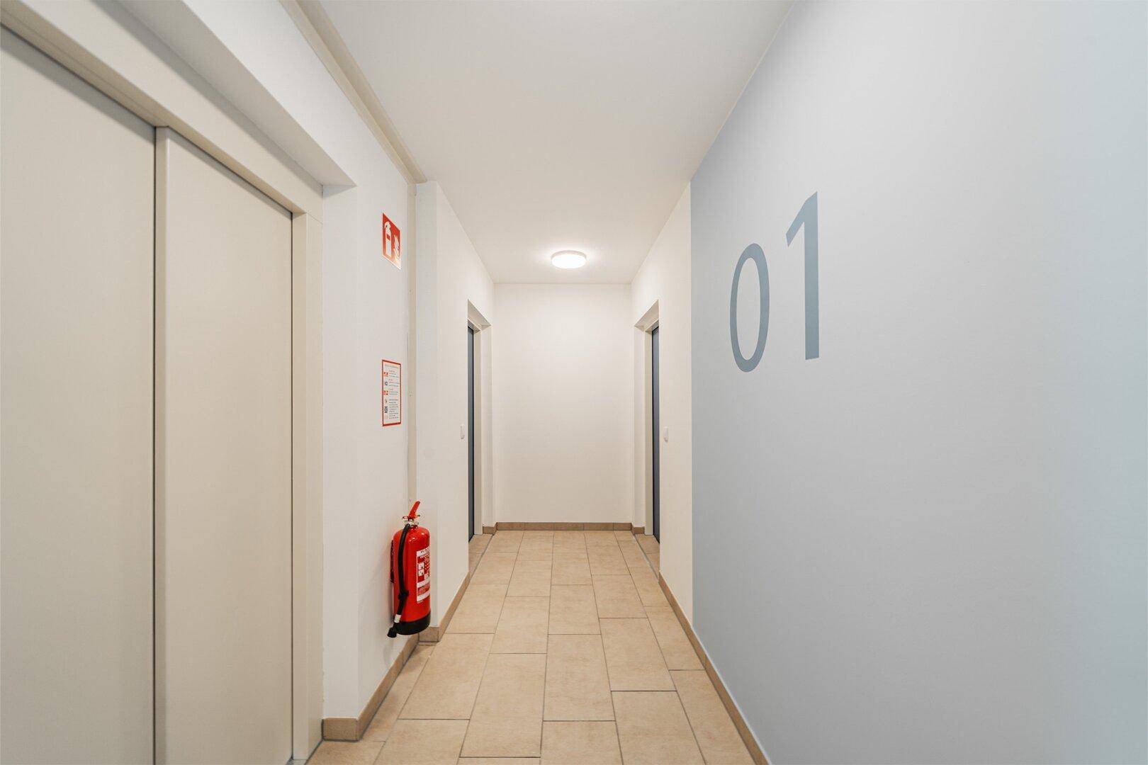 Heller Flur im Mehrfamilienhaus mit Aufzug, Fliesenboden und Feuerlöscher.