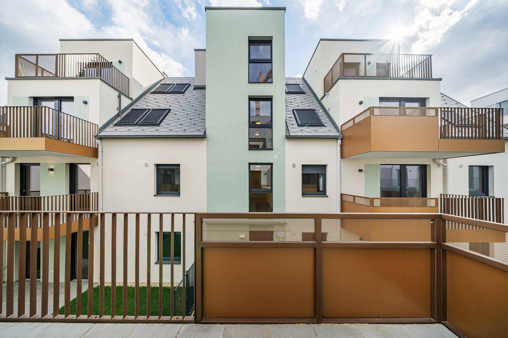 Rückansicht eines modernen Wohngebäudes mit Balkonen, Dachfenstern und einem kleinen Gartenbereich.