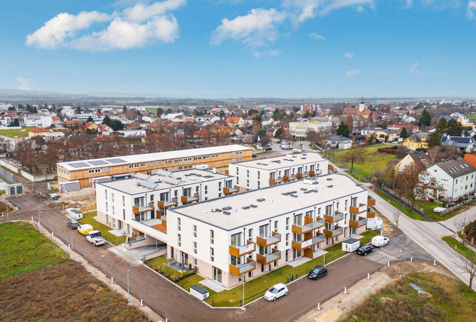 Weitläufige Luftaufnahme einer modernen Wohnsiedlung mit Flachdächern und Balkonen in einer Stadtlandschaft.