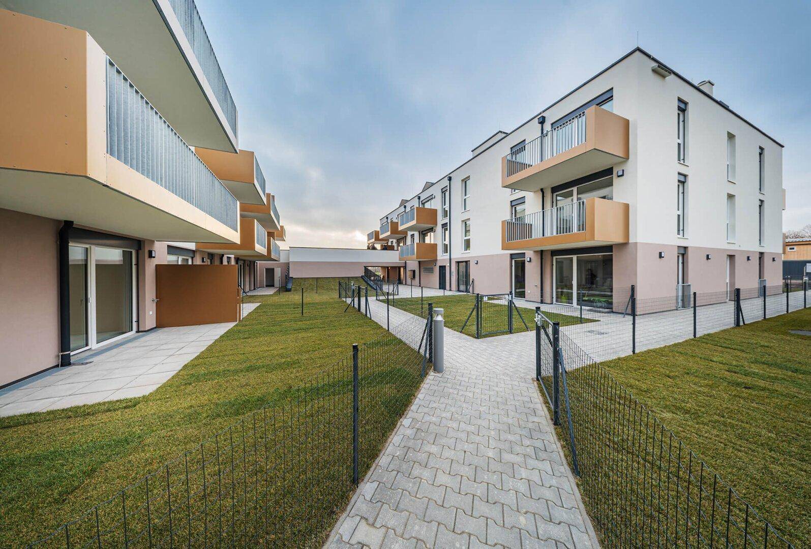 Ansicht der modernen Wohngebäude mit gepflegten Rasenflächen und privaten Terrassen im Erdgeschoss.