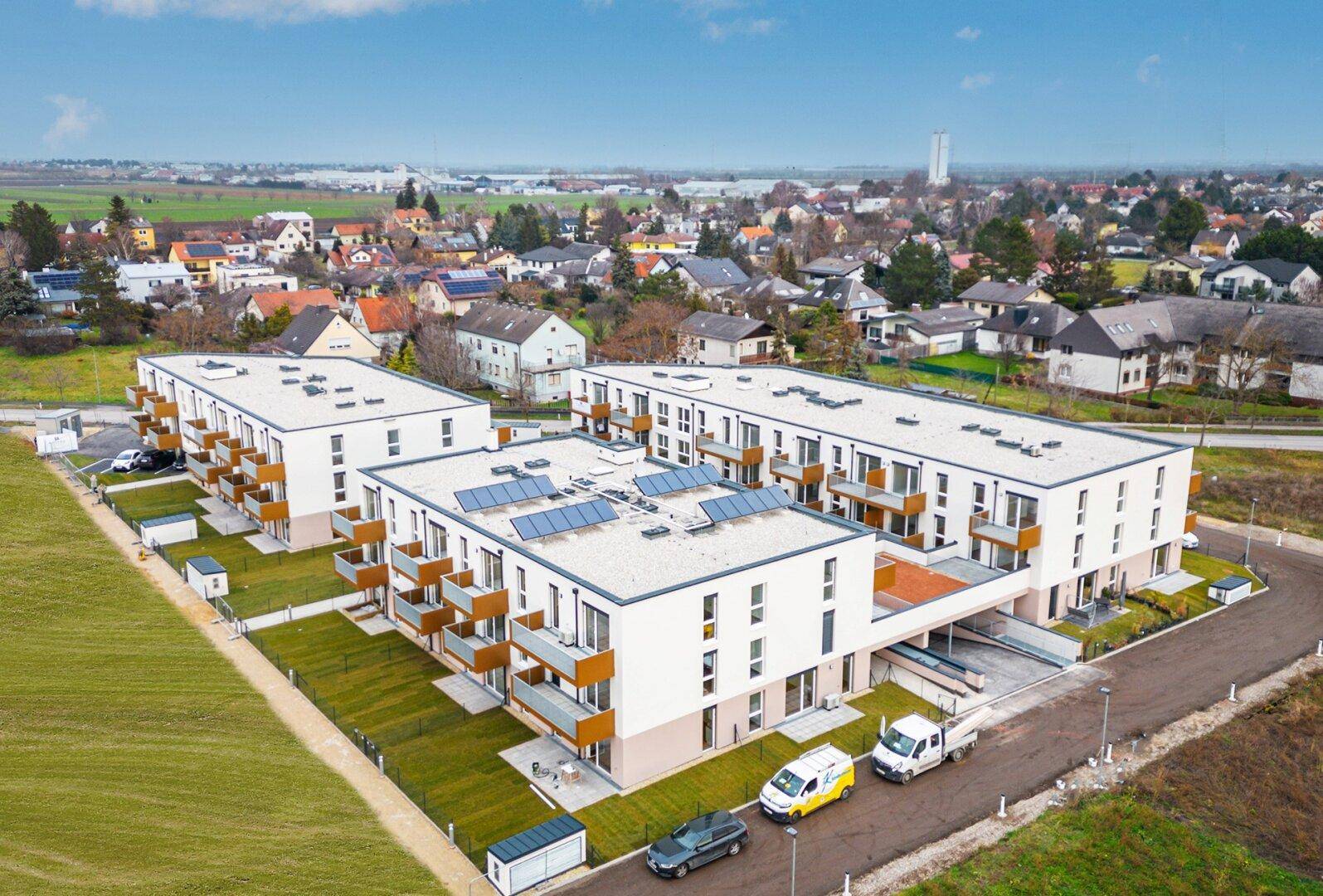 Vogelperspektive auf eine moderne Wohnanlage mit Solarpaneelen auf den Dächern und Balkonen.