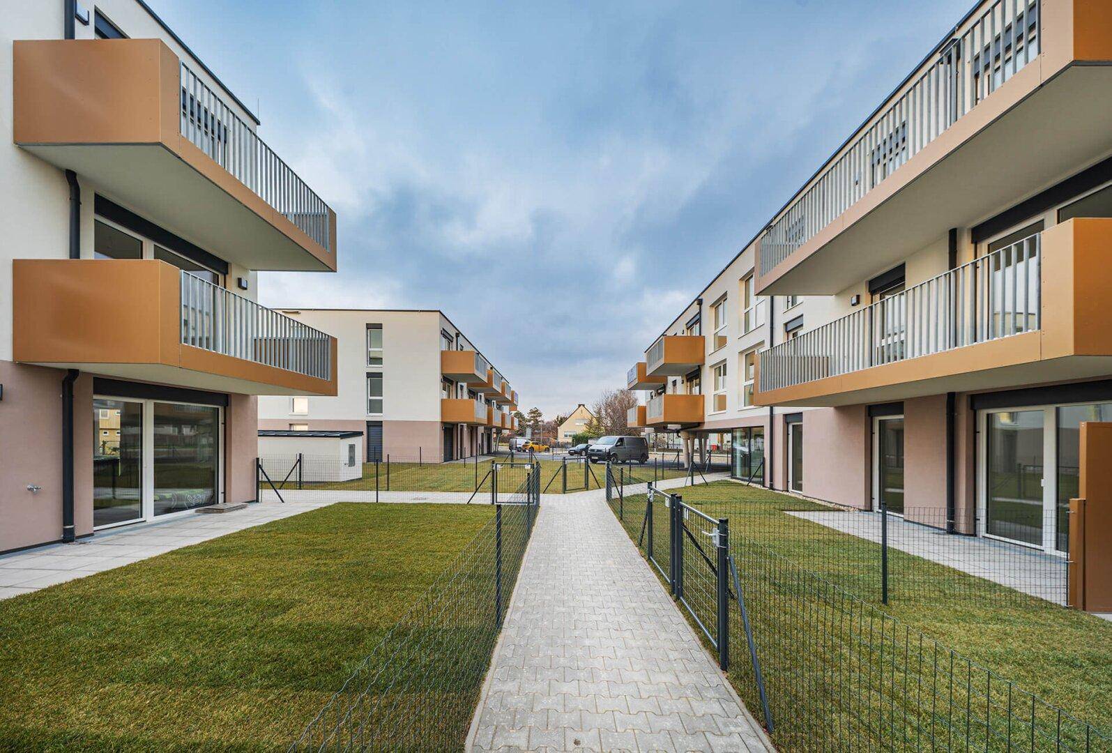 Blick zwischen modernen Wohngebäuden mit gepflegten Rasenflächen und privaten Terrassen im Erdgeschoss.
