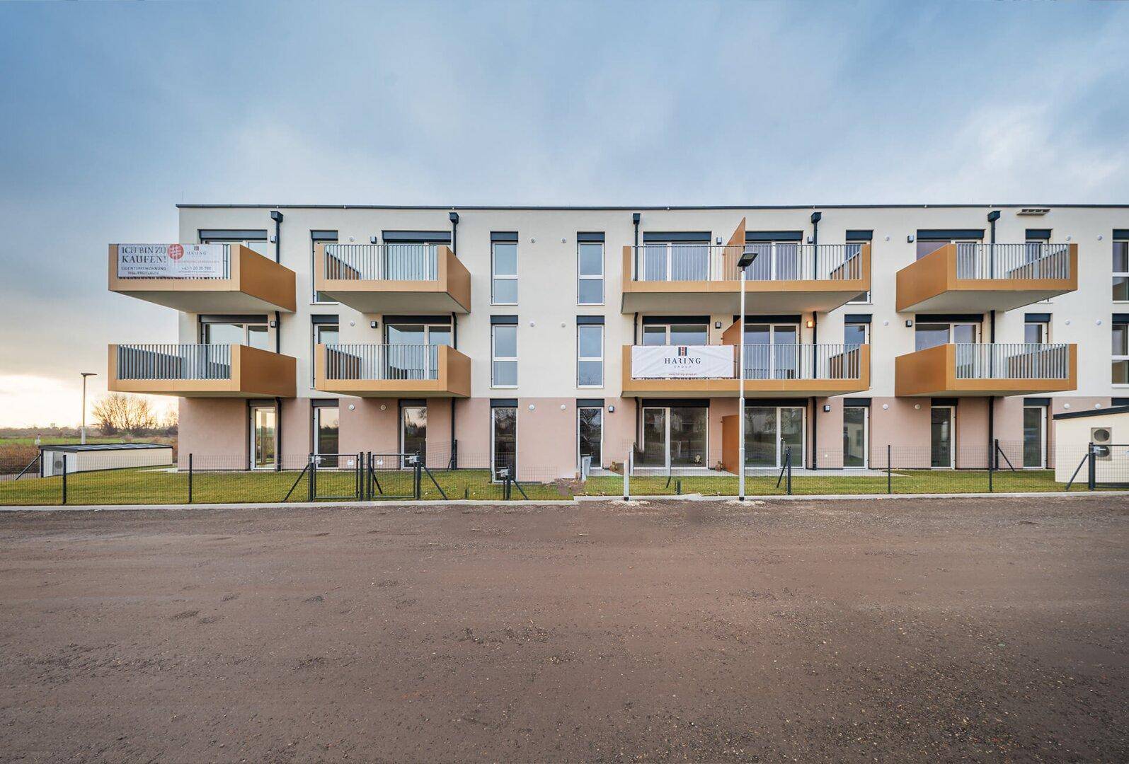 Fassade eines modernen Wohngebäudes mit Balkonen, großen Fenstern und Werbebannern.