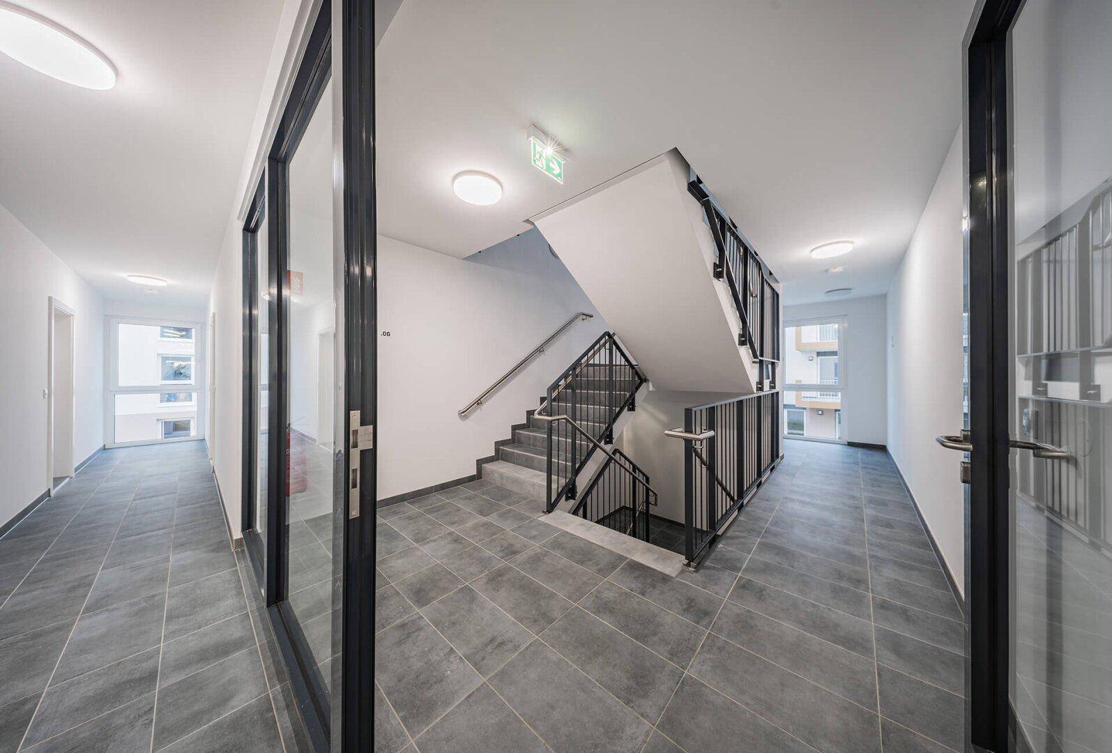 Geräumiges Treppenhaus mit Fliesenboden und modernem Geländer, das zu den oberen Etagen führt.
