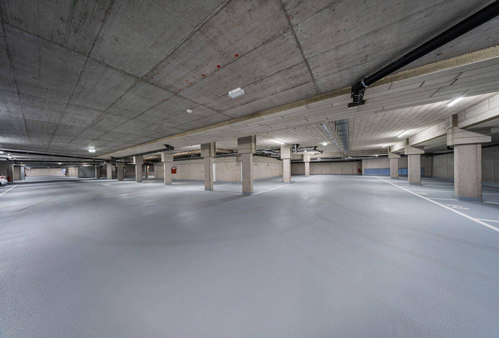 Große Tiefgarage mit zahlreichen Stellplätzen und Betonwänden, gut beleuchtet.