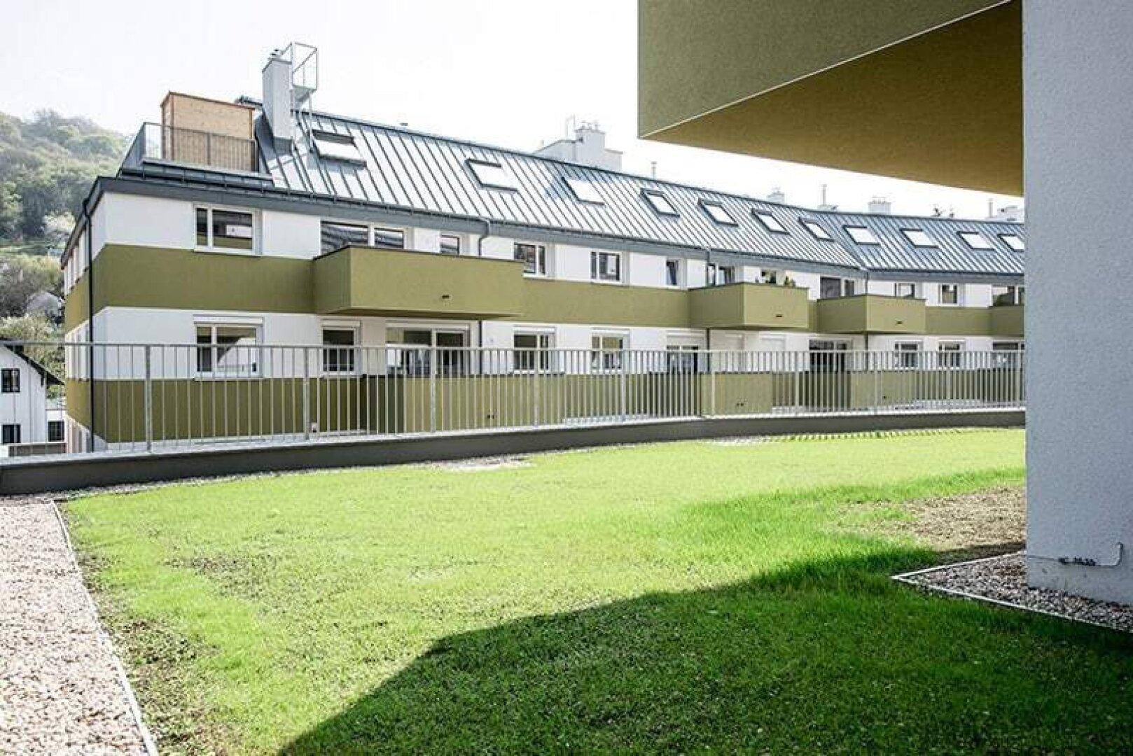Weitläufige Rasenfläche vor den modernen Wohngebäuden mit Dachfenstern.