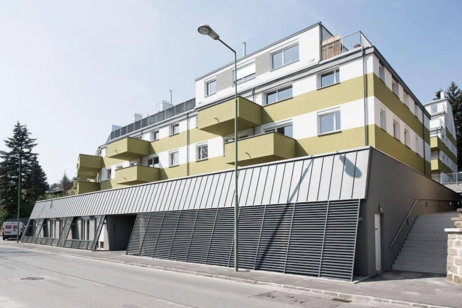 Moderne Fassade eines Wohngebäudes mit Tiefgaragenzufahrt von der Straße aus.