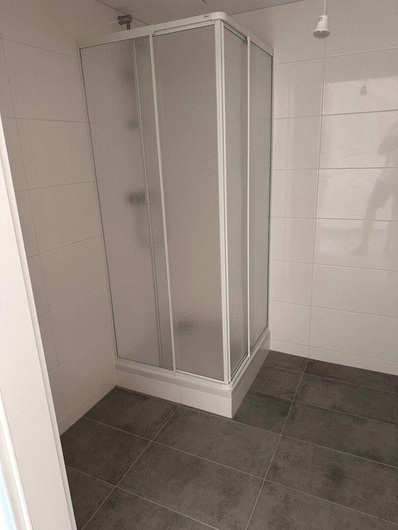 Modernes Badezimmer mit Duschkabine, weißen Wandfliesen und dunklem Boden.