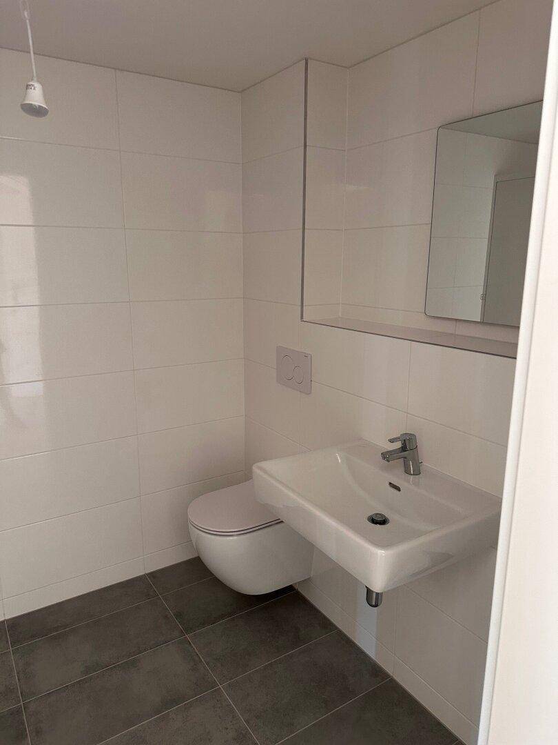 Helles Badezimmer mit wandhängendem WC, Einzelwaschbecken und Spiegel.