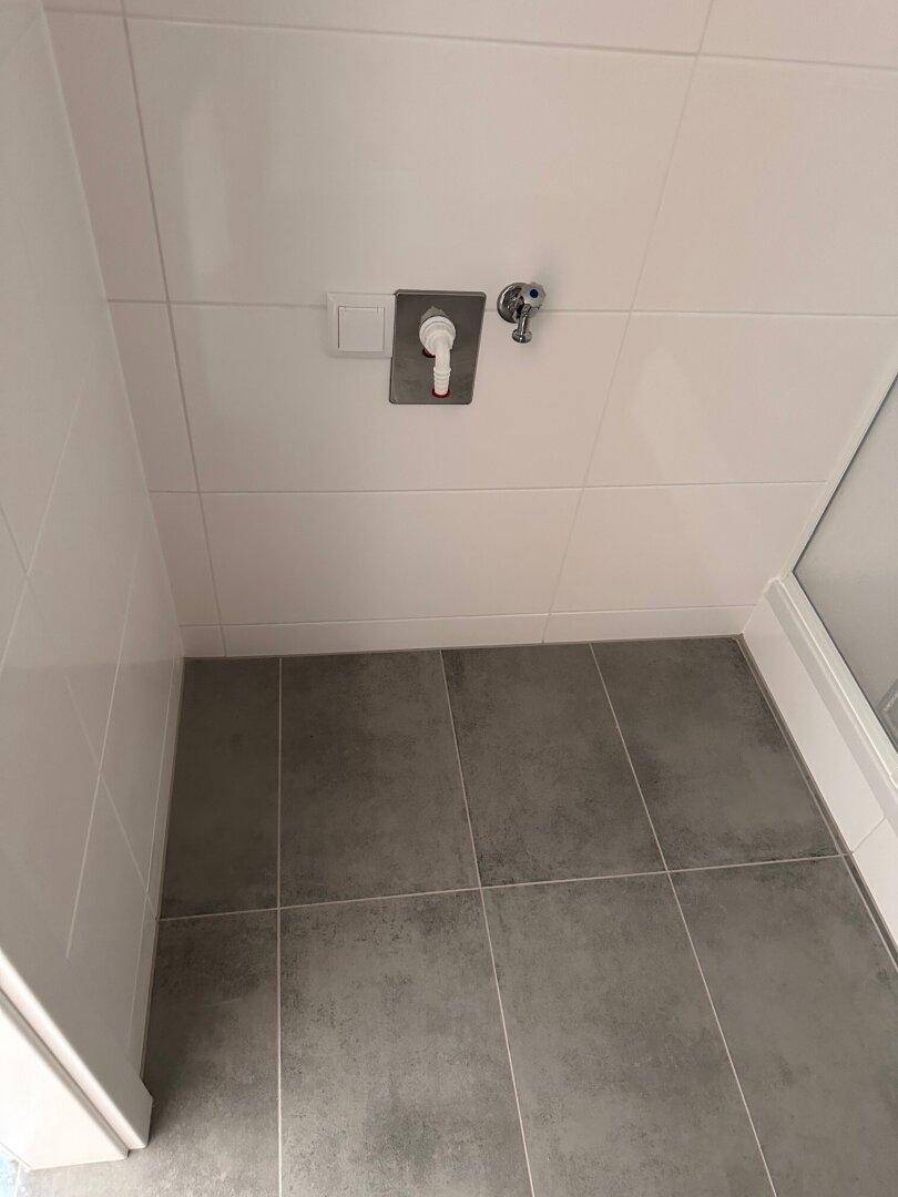 Detailansicht des Badezimmers mit weißen Fliesen und Anschluss für Waschmaschine.