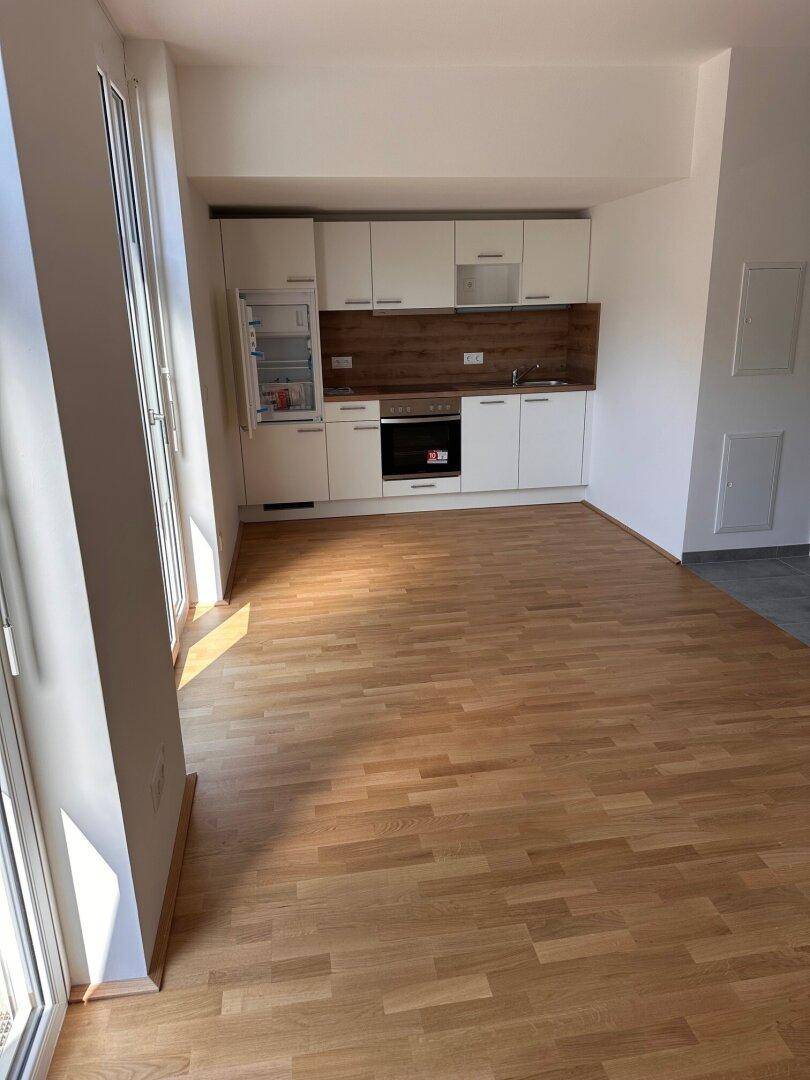 Offene Küche mit weißen Schränken, Holzarbeitsplatte und hellem Holzboden.