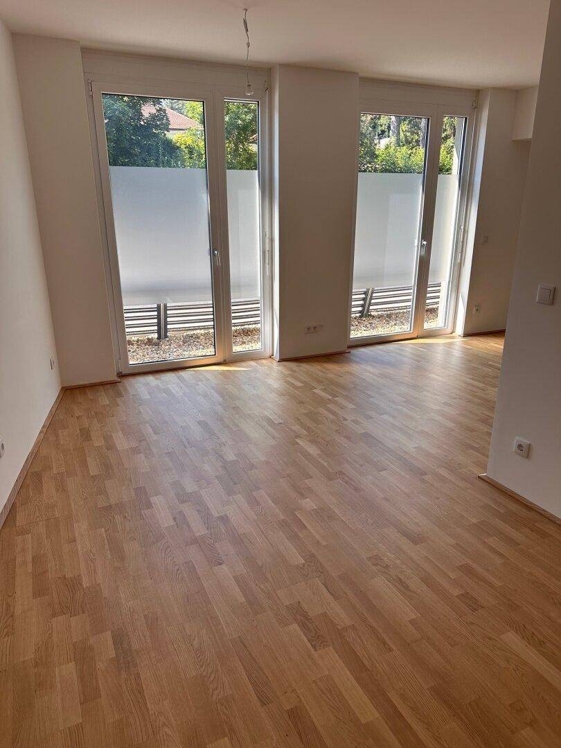 Geräumiger Wohnbereich mit Holzboden und zwei großen Fenstertüren für viel Licht.