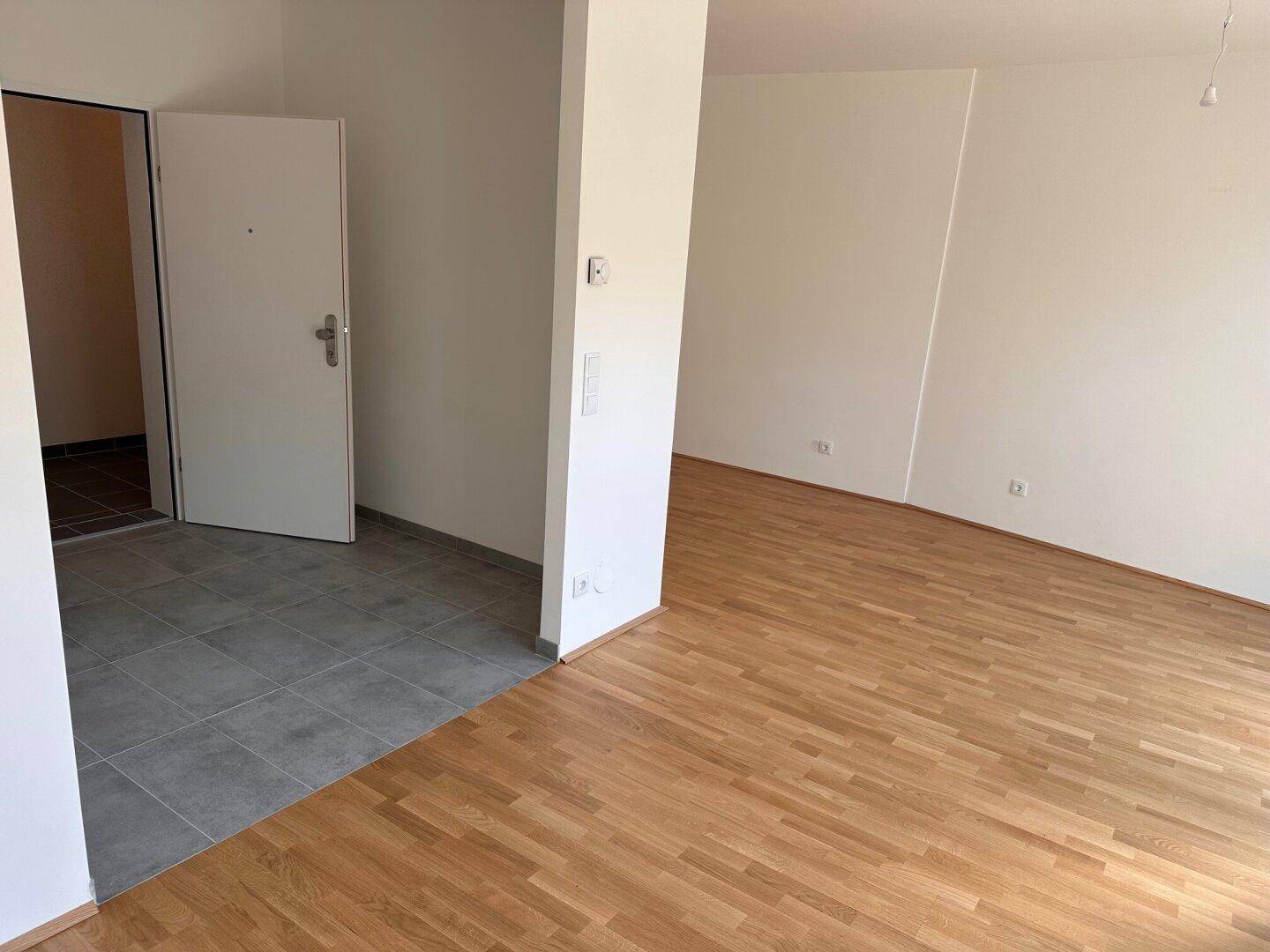 Blick vom Wohnbereich zum Eingang mit Übergang von Holzboden zu modernen Fliesen.