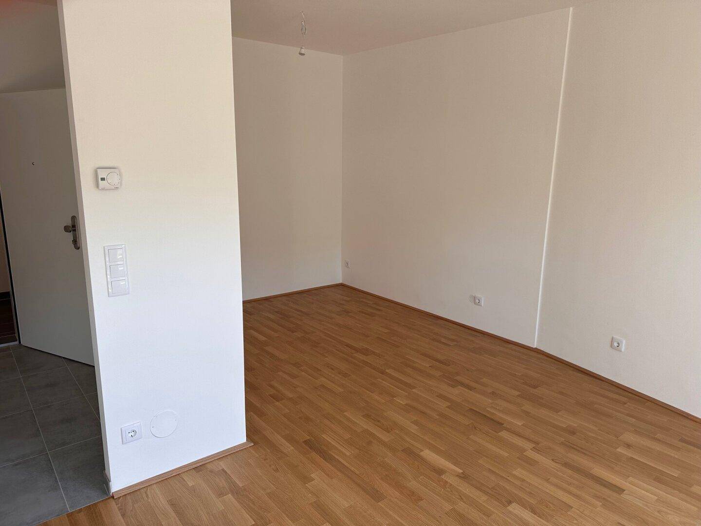 Heller und leerer Wohnraum mit Holzboden und weißen Wänden, bereit zur Einrichtung.