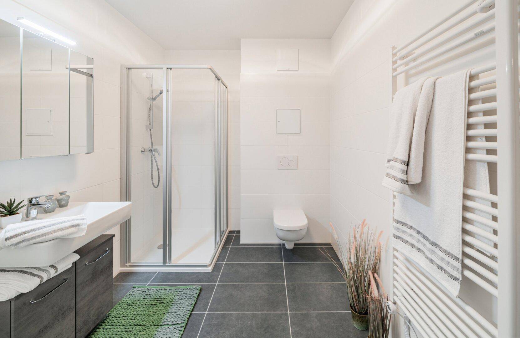 Modernes Badezimmer mit Duschkabine, Wand-WC und beheiztem Handtuchhalter.
