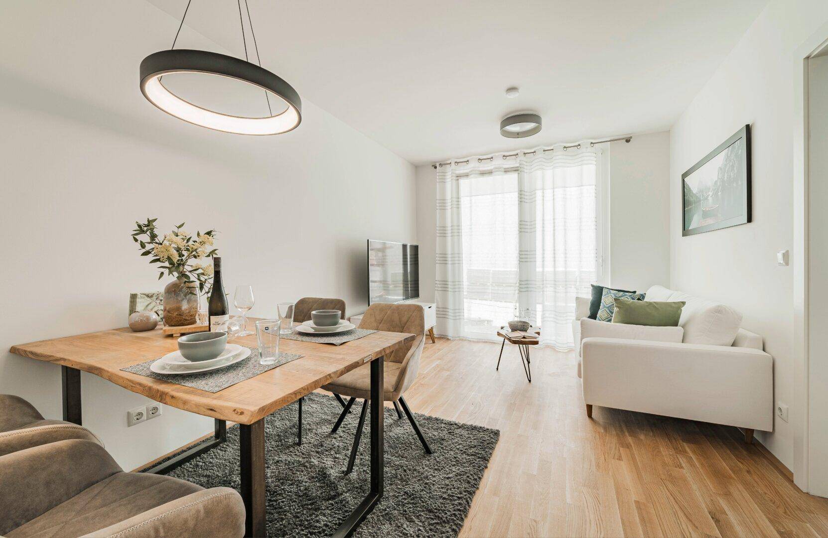 Gemütlicher Wohn-Essbereich mit Holztisch, bequemen Sofas und Zugang zu einem Balkon.