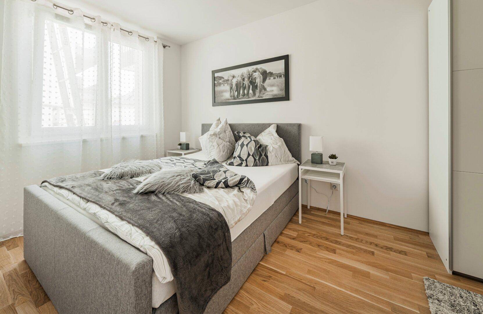 Helles Schlafzimmer mit Doppelbett, Holzboden und großem Fenster für viel Tageslicht.