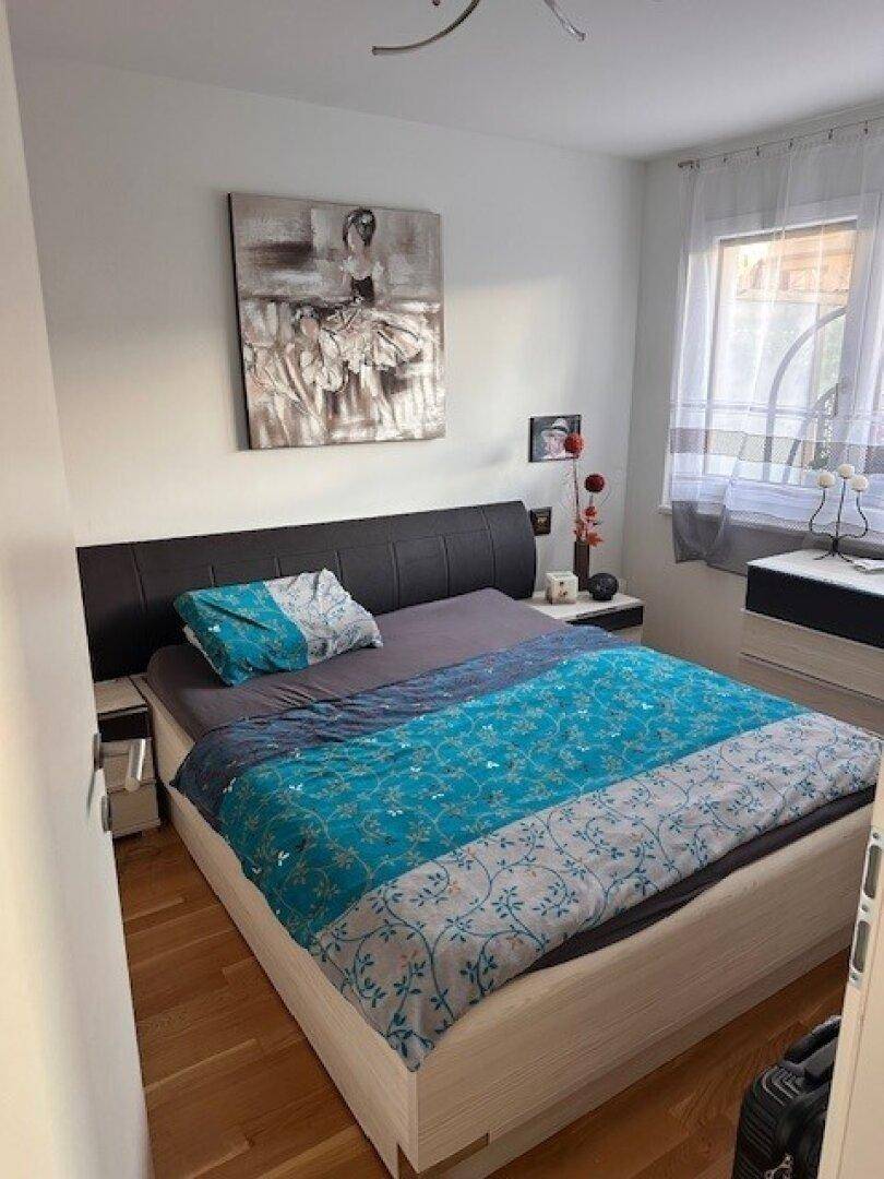 Gemütliches Schlafzimmer mit Holzboden, Doppelbett und Fenster mit Vorhängen.