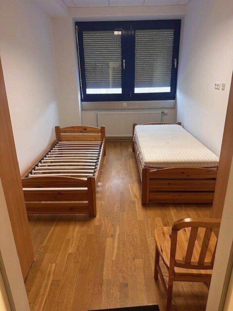 Schlafzimmer mit zwei Einzelbetten, Holzmöbeln und Fenster mit Rollläden.