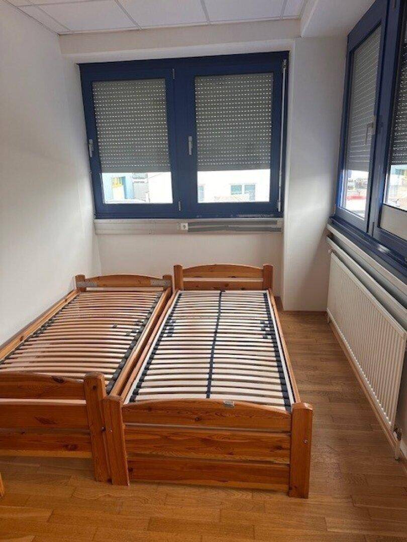 Schlafzimmer mit zwei Holzbetten und Fenstern mit geschlossenen Rollläden.
