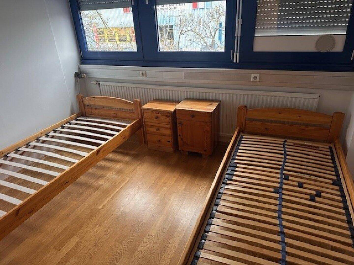Schlafzimmer mit zwei Einzelbetten, Nachttischen und Fenstern mit Rollläden.