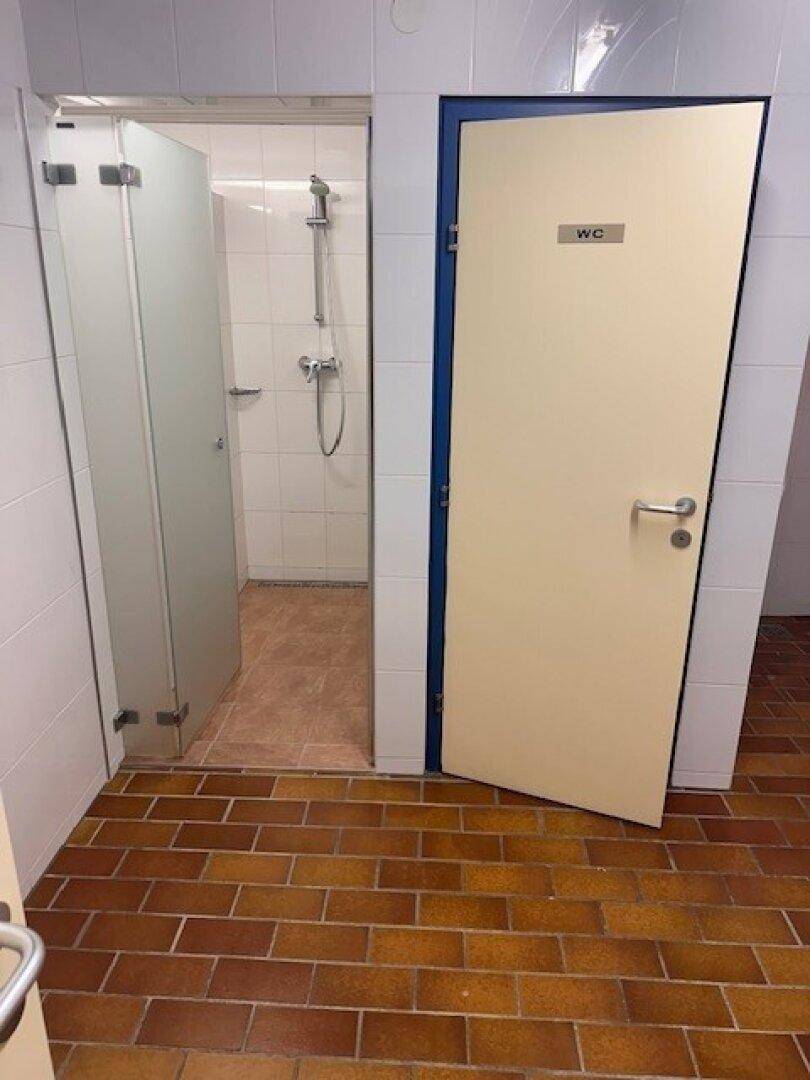 Duschbereich mit weiß gefliesten Wänden und braunem Fliesenboden.
