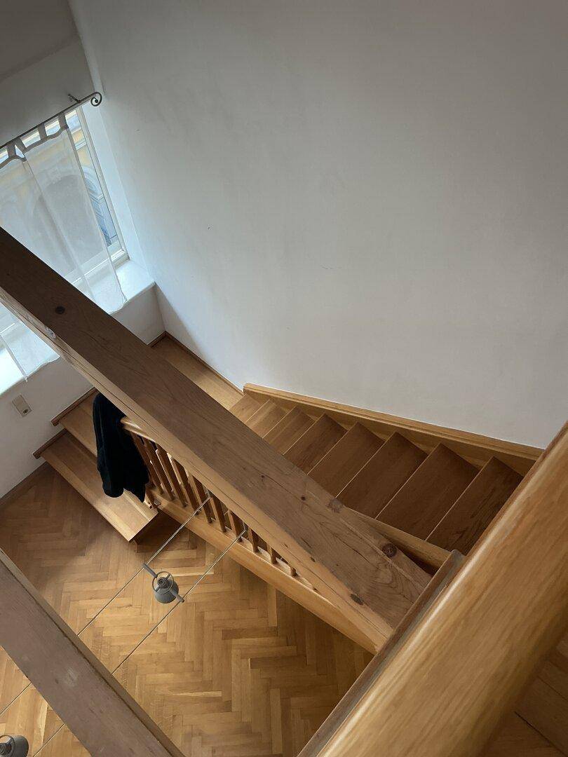 Helle Holztreppe mit Geländer verbindet die Etagen und bietet einen Blick nach unten.