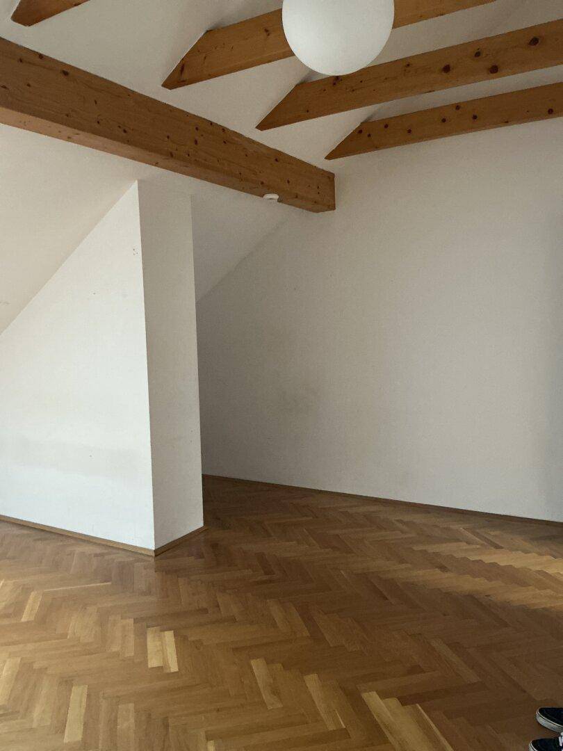 Leerer Raum im Dachgeschoss mit Holzbalken und Parkettboden, bereit zur individuellen Gestaltung.
