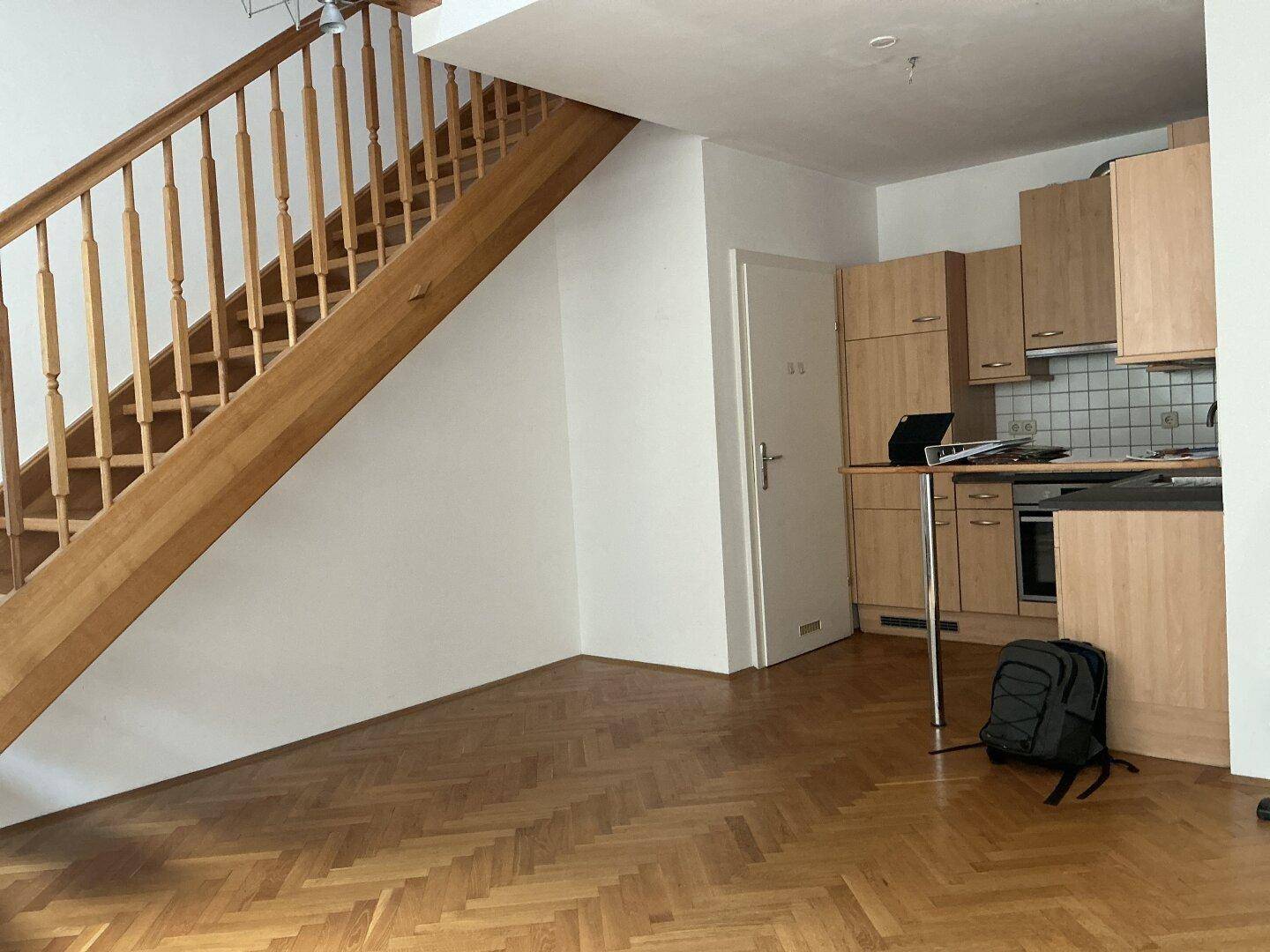 Offener Bereich mit Parkettboden, Treppe und integrierter Küchenzeile, bereit zur Einrichtung.