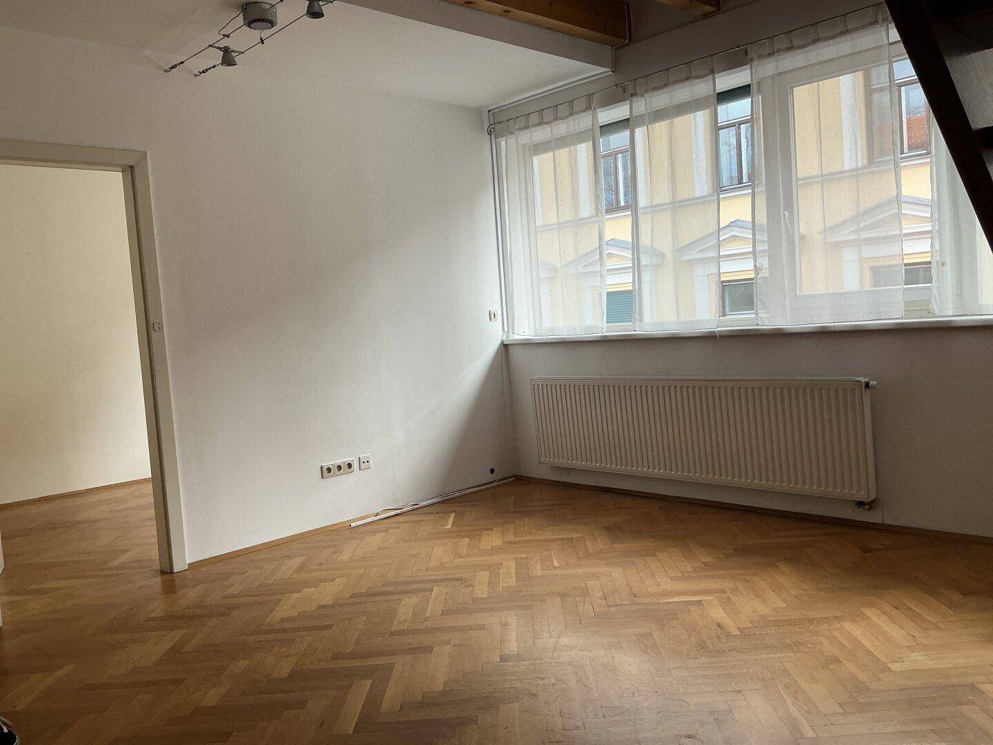 Leerer Raum mit Parkettboden, großem Fenster und Heizkörper, bereit zur individuellen Gestaltung.
