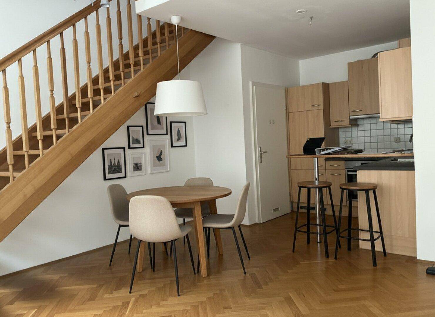 Offener Wohn-Essbereich mit Holzboden, Esstisch und integrierter Küchenzeile unter der Treppe.