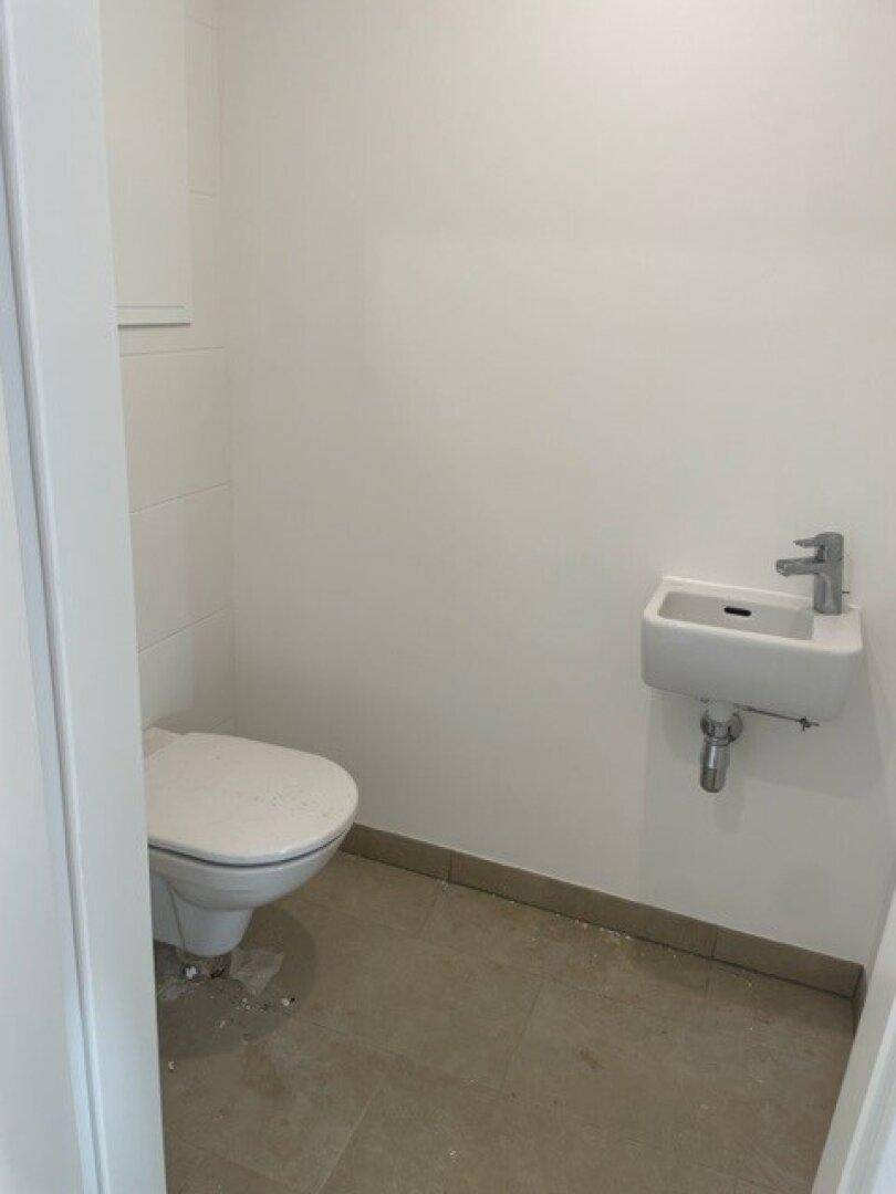 Modernes Gäste-WC mit Wand-WC und kleinem Waschbecken, ausgestattet mit hellen Fliesen.