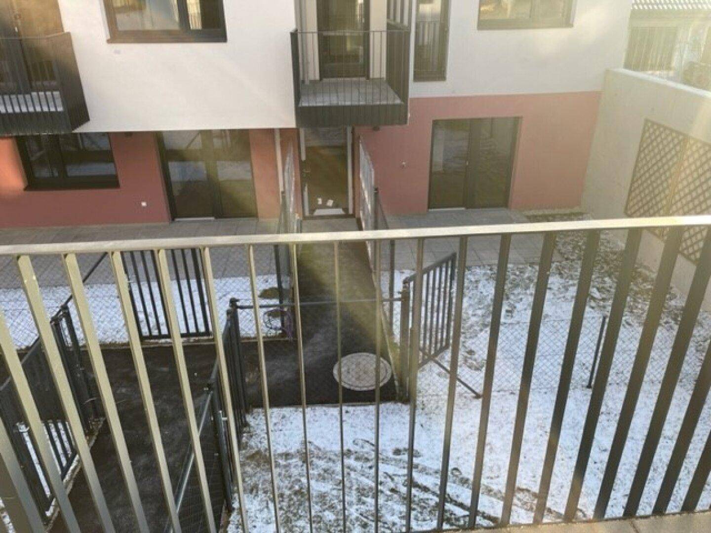 Blick vom Balkon auf einen schneebedeckten Innenhof und die Fassade des Gebäudes.