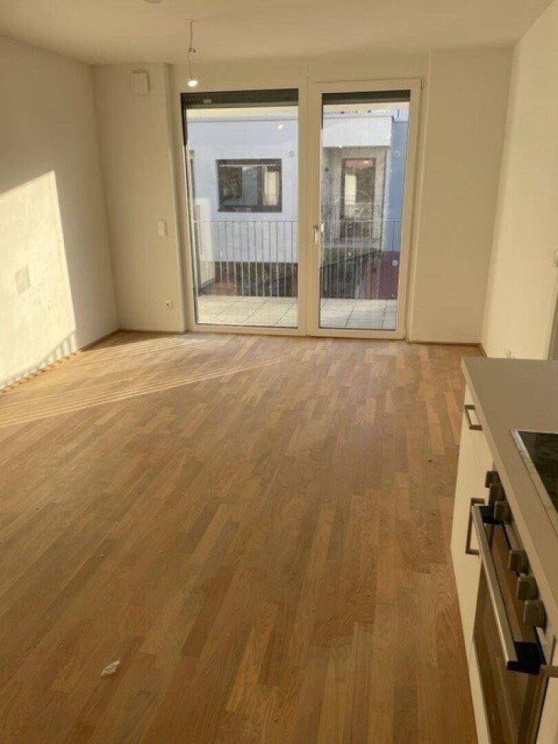 Wohnbereich mit Parkettboden und Zugang zu einem Balkon, der viel Tageslicht hereinlässt.