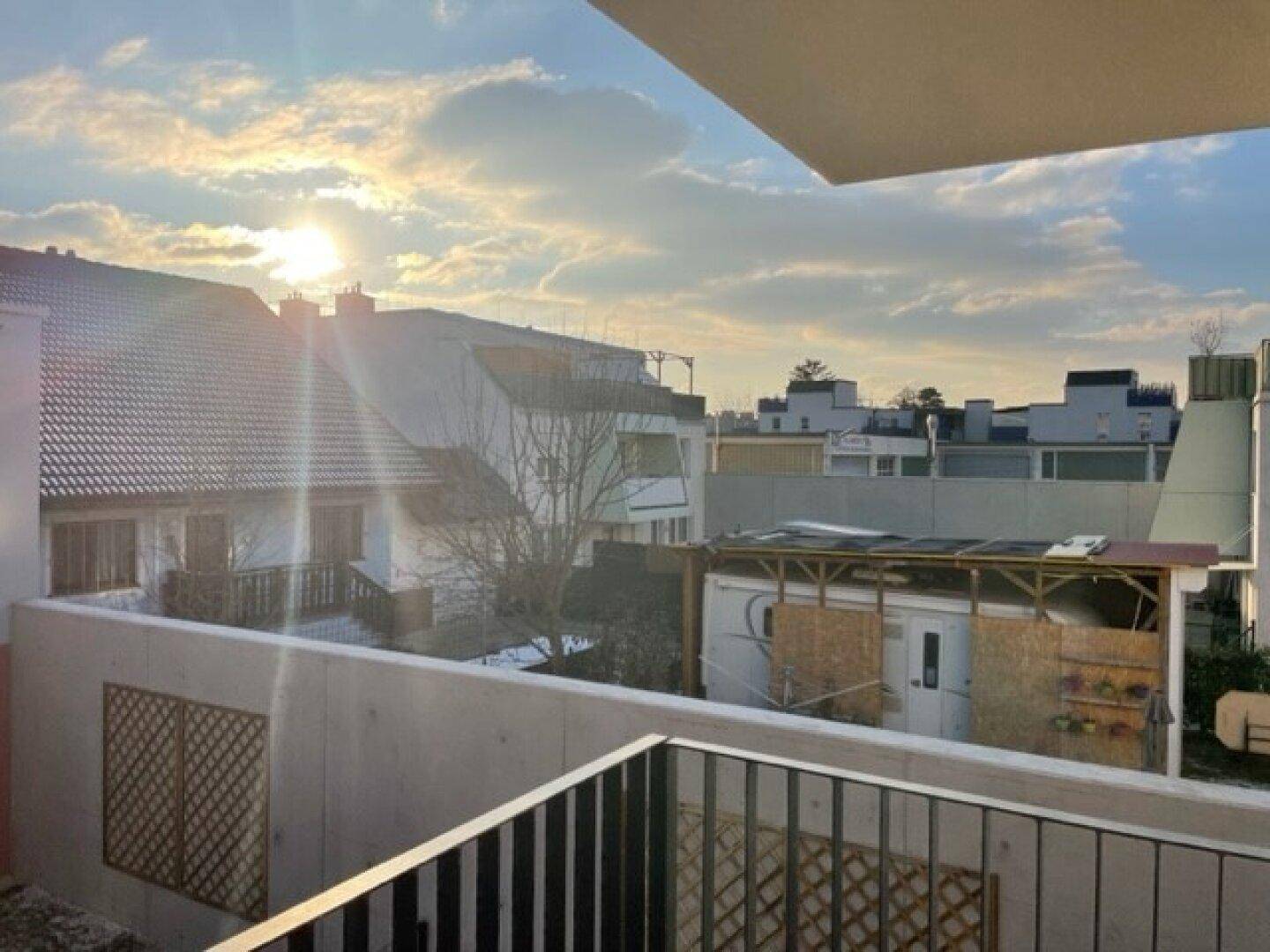 Sonniger Ausblick vom Balkon auf die umliegenden Gebäude und den Himmel bei Sonnenuntergang.