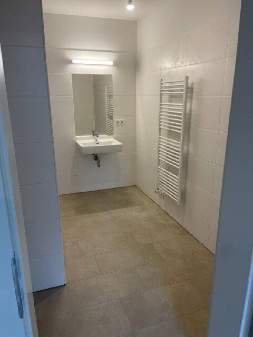 Modernes Badezimmer mit Waschbecken, Spiegel und Handtuchheizkörper, ausgestattet mit hellen Fliesen.