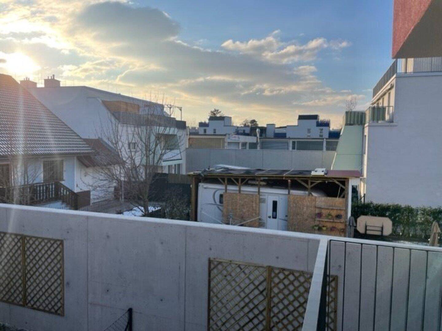 Sonniger Ausblick vom Balkon auf die umliegenden Gebäude und den Himmel bei Sonnenuntergang.